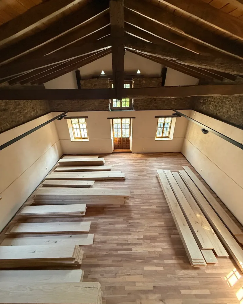 Tablas Dinesen Layers HeartOak extendidas para aclimatar en una sala con cubierta de madera y muros de piedra