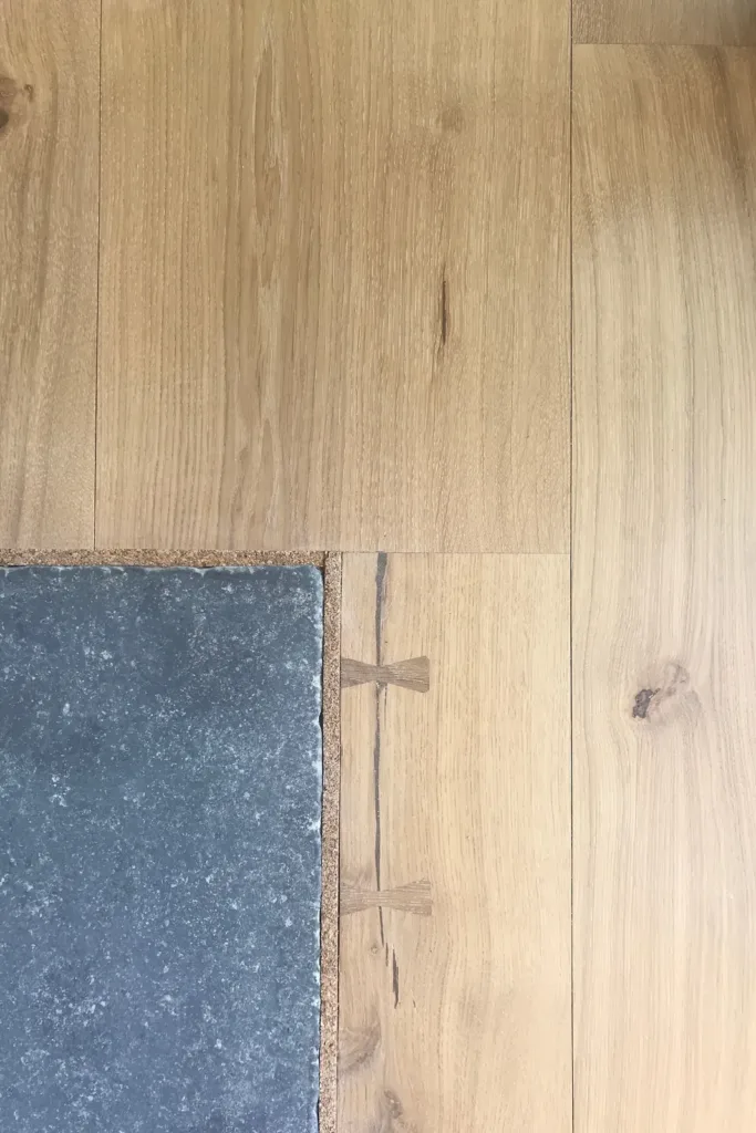 Esquina de una losa de piedra gris rodeada por una junta de corcho en su encuentro con las tablas de roble; en la tabla de al lado, una grieta cosida con dos mariposas