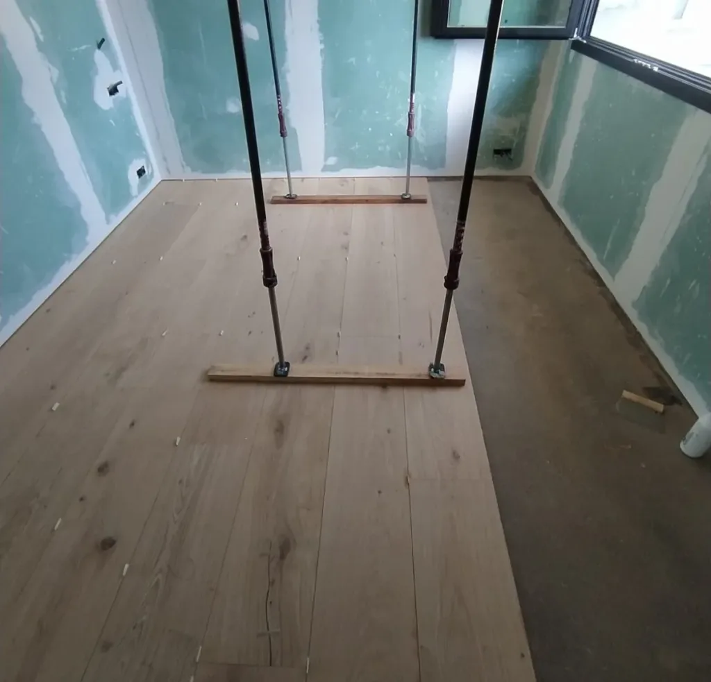 Tablas de roble recién colocadas en una estancia en obra, apretadas con dos pares de puntales sobre listones; a la derecha, la solera todavía sin cubrir