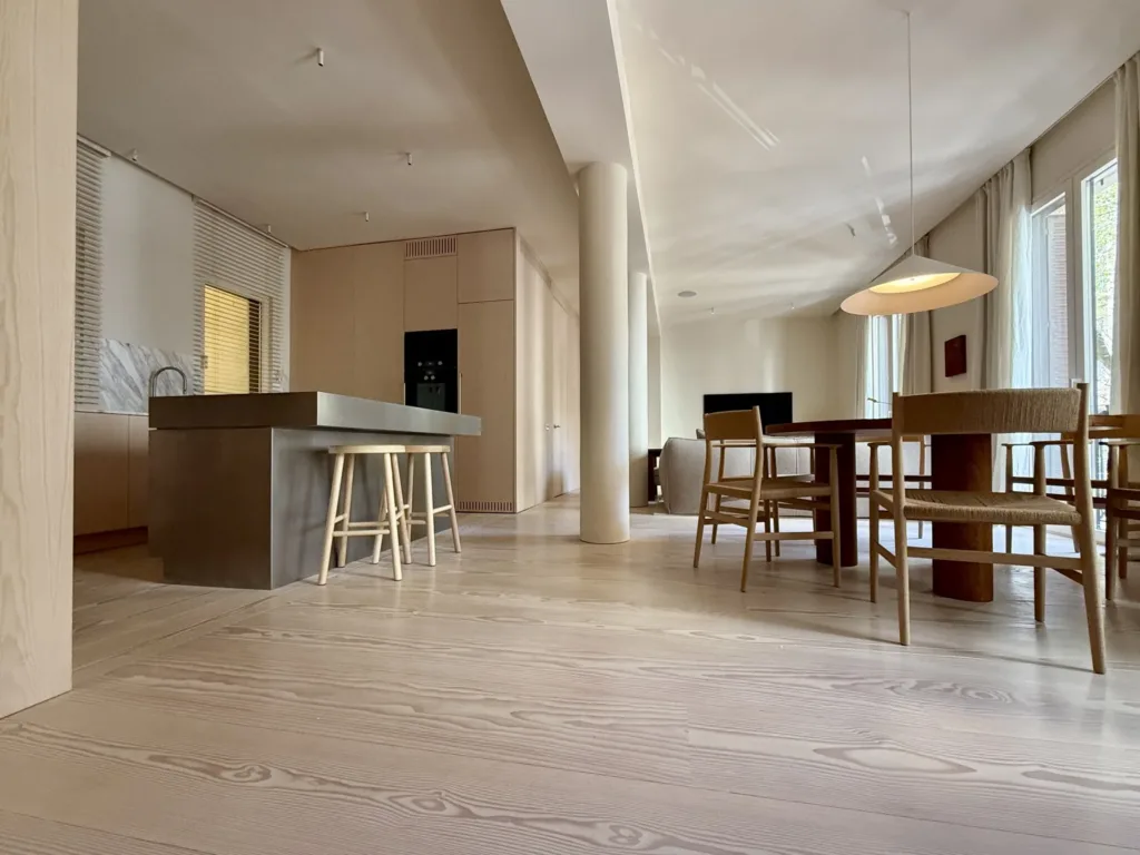Cocina abierta de Casa Ambrose con isla de acero, pilar y mesa de comedor sobre suelo Dinesen Layers Douglas Classic
