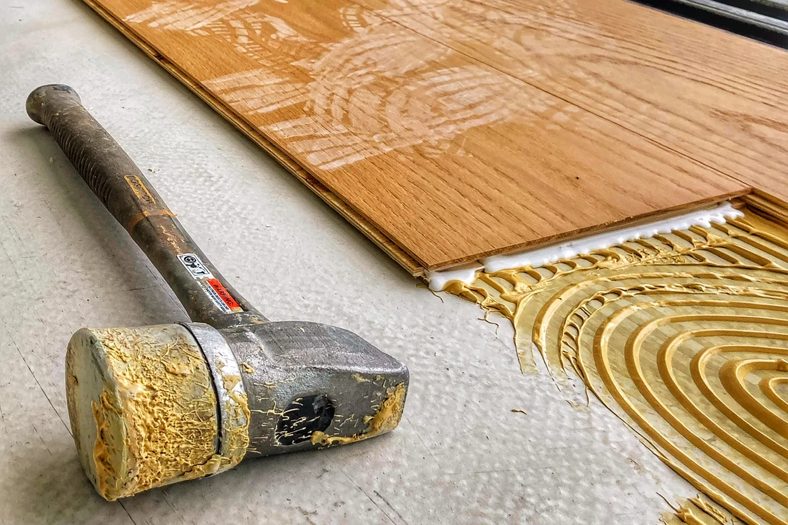 Tabla encajándose sobre el adhesivo peinado con llana dentada, con taco de golpeo y maza