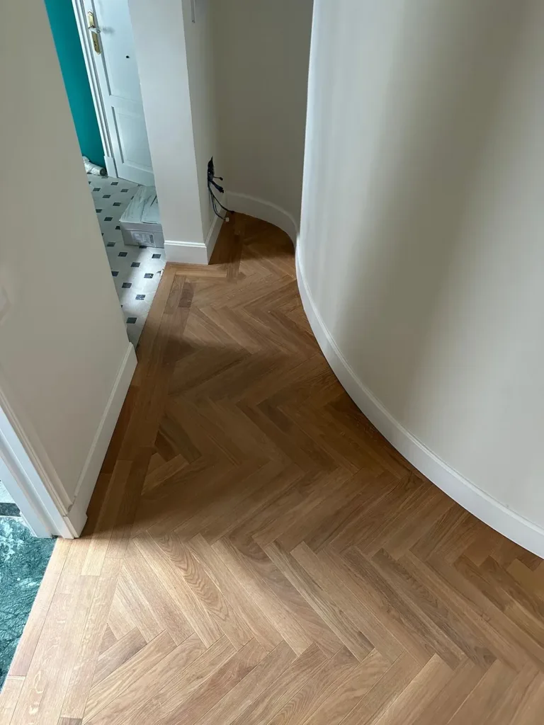 Suelo de espiga que sigue el muro curvo de un pasillo, con el rodapié también curvo