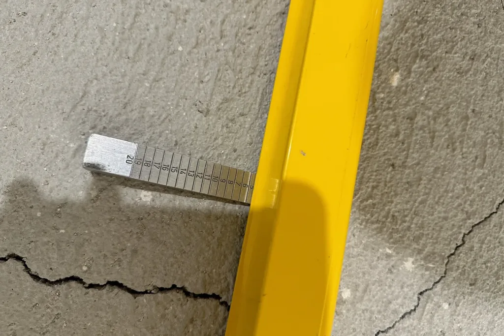 Galga de cuña bajo la regla de 2 m sobre una solera: la flecha supera los 3 mm que admite la UNE 56810:2023