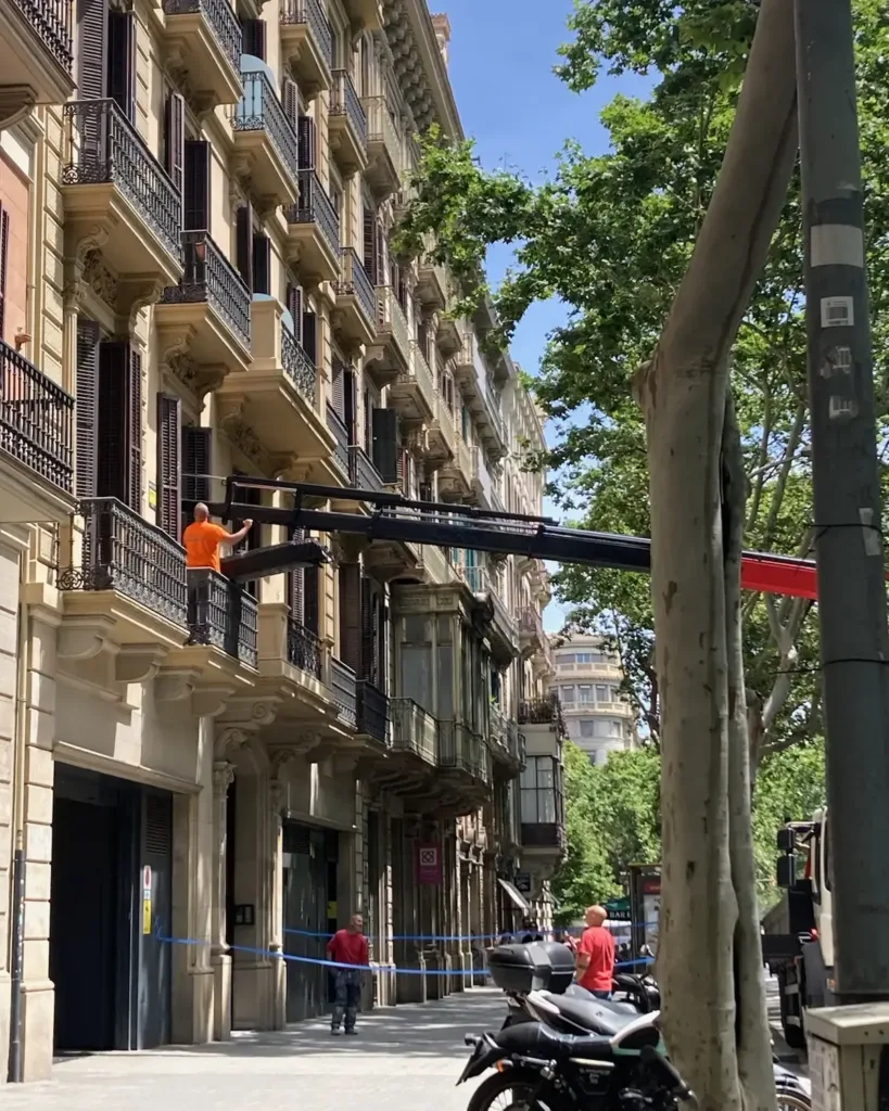 Brazo de la grúa entregando un paquete de tablas Douglas de 7,5 m en el balcón de la vivienda, con la acera acotada