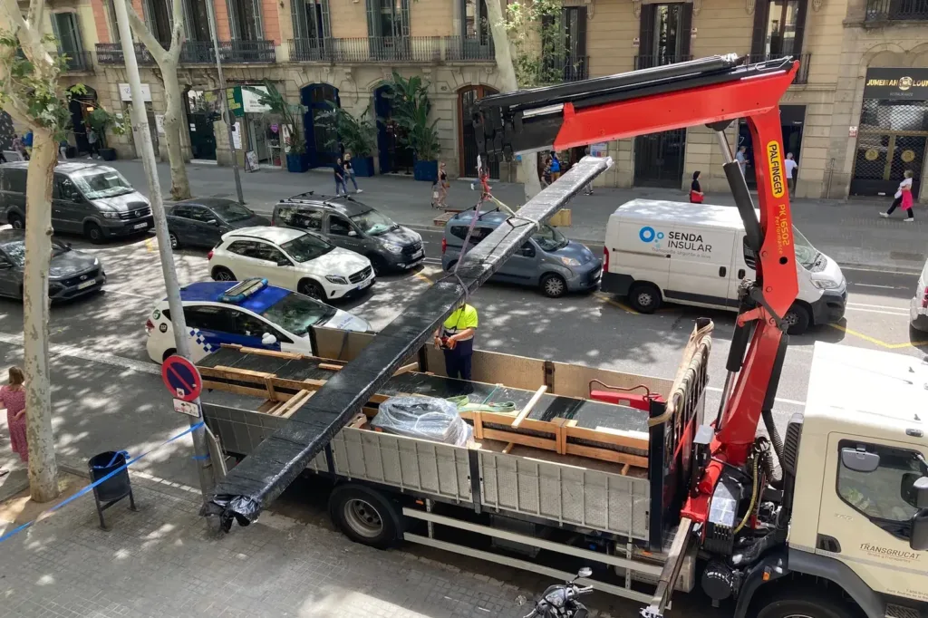 Camión grúa izando desde la calle un paquete de tablas Douglas de gran longitud hasta la ventana de la vivienda
