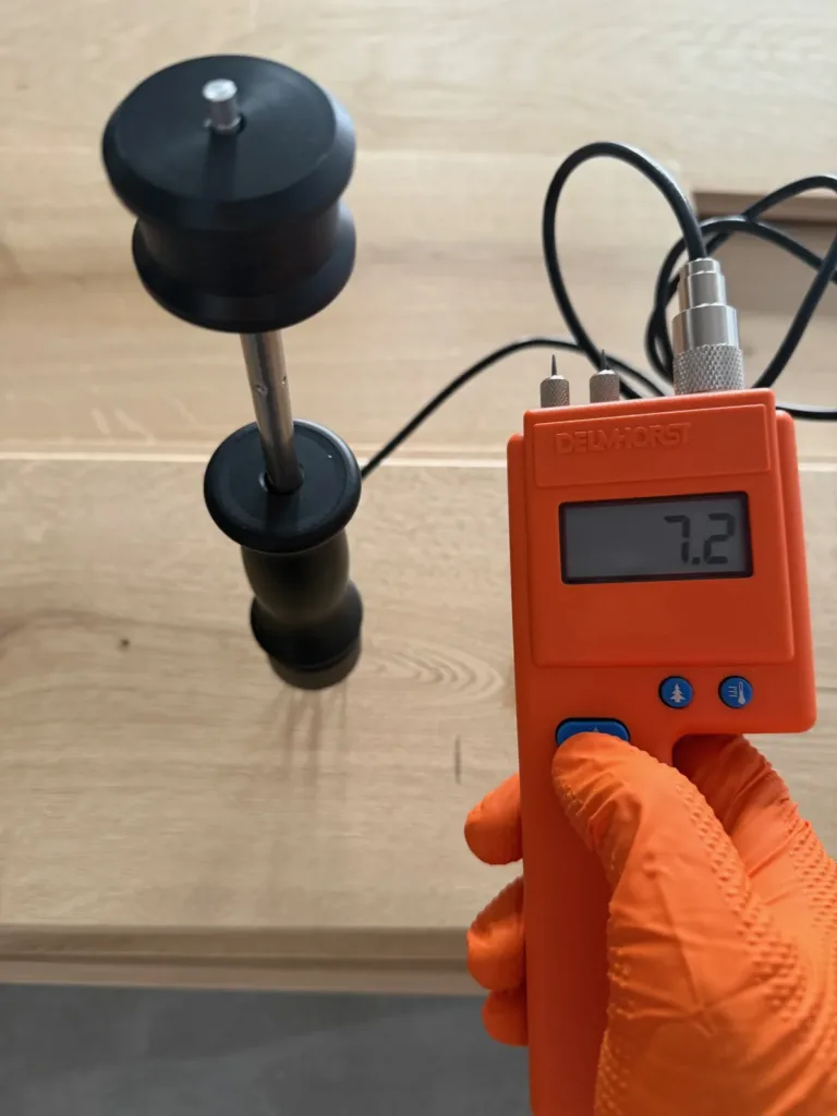 Higrómetro Delmhorst naranja con electrodo de martillo clavado en una tabla de roble; la pantalla marca 7,2