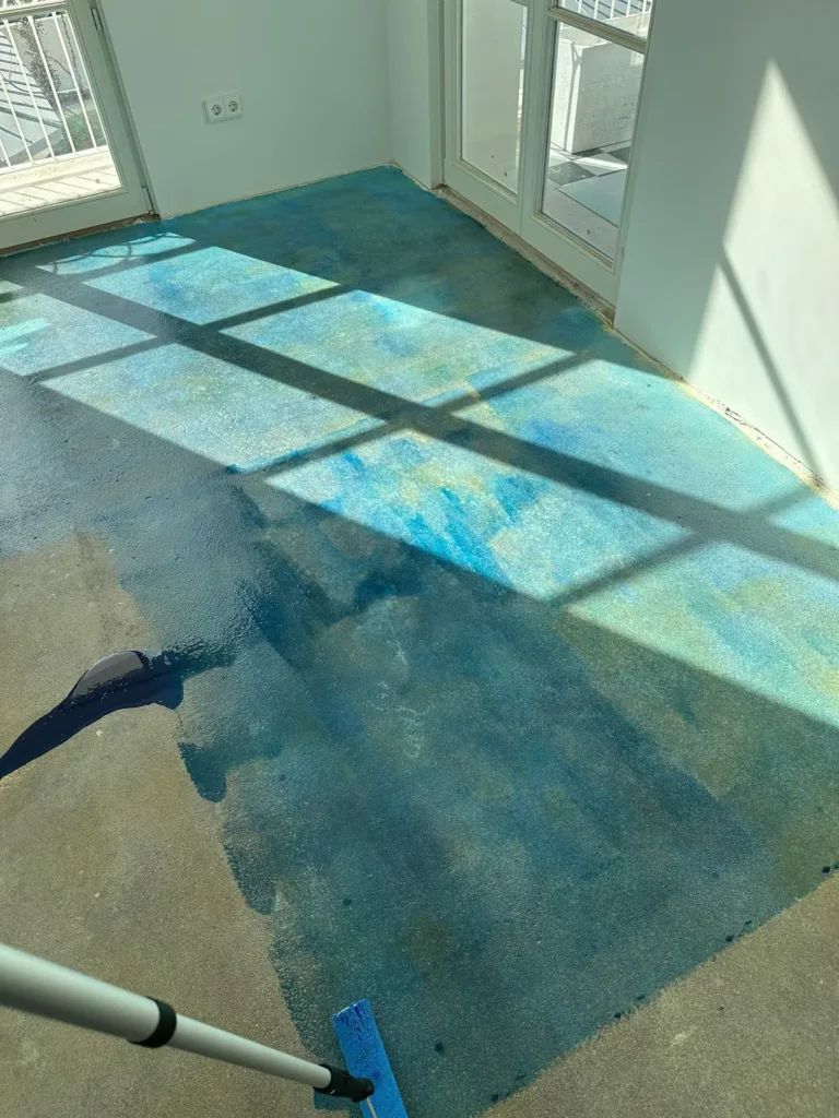 Rodillo extendiendo imprimación azul sobre la solera de una estancia; en primer plano, solera todavía sin tratar