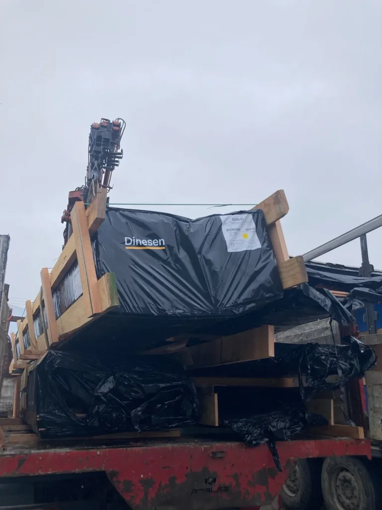Palé de tablas Dinesen embalado en plástico negro sobre un camión grúa
