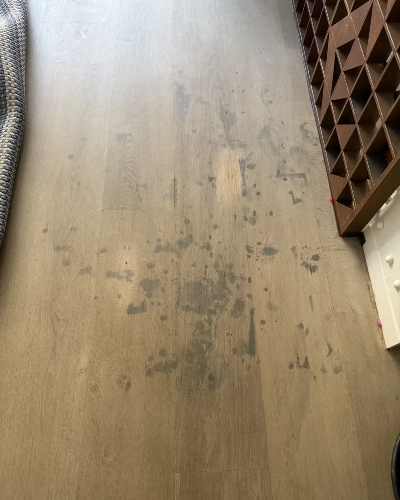 Salpicaduras grises y negras sobre un suelo de roble con acabado claro, junto a una estantería de acero corten: reacción de taninos, agua y hierro