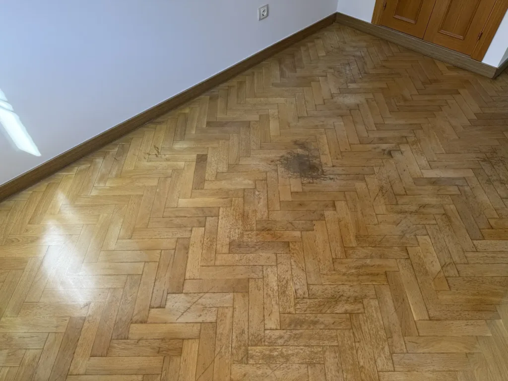 Parquet de roble en espiga antes del lijado, con arañazos, suciedad incrustada en el barniz y una mancha oscura frente al armario, piso con mirador en Madrid
