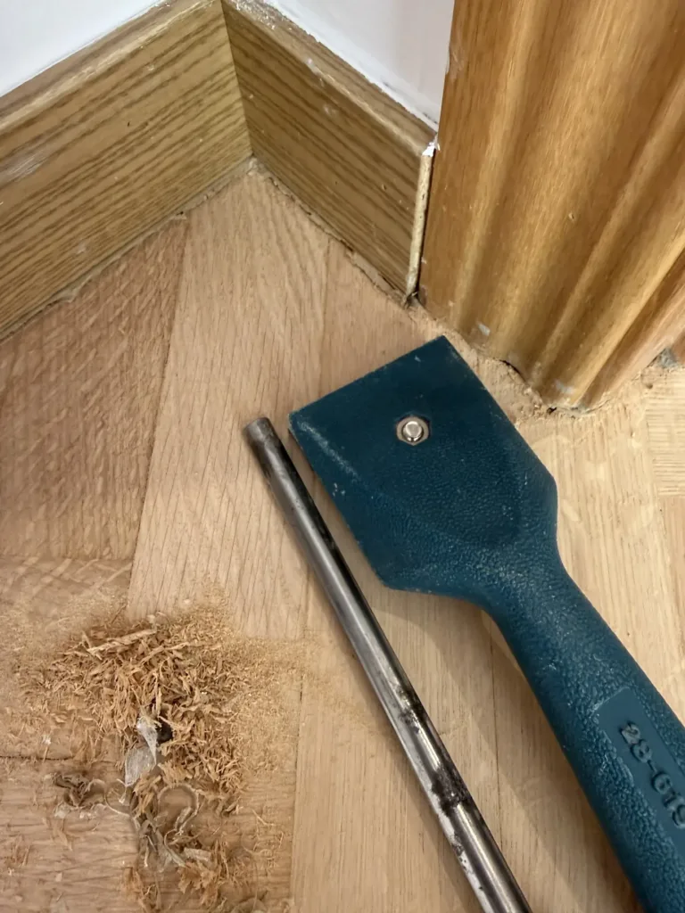 Virutas de barniz y madera retiradas con rasqueta en el rincón bajo el tapajuntas de la puerta, con el rodapié en su sitio, piso con mirador en Madrid