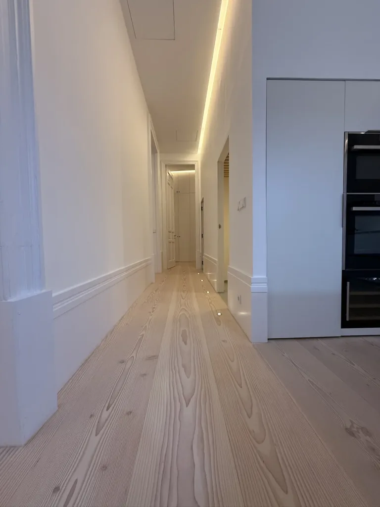 Pasillo con luz lineal y focos de suelo sobre las tablas Dinesen Douglas, vivienda en el barrio de Palacio (Madrid)