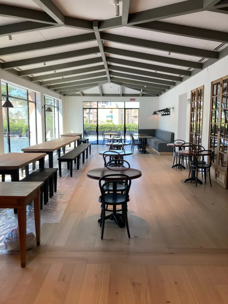Comedor del restaurante italiano del Campus Acciona, con techo de vigas, mesas de bistró y suelo de roble terminado