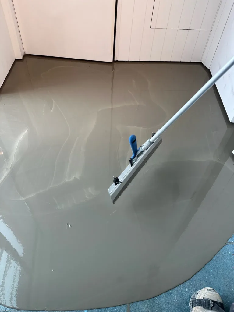 Extendido del recrecido autonivelante Bona H600 con una llana dentada de mango largo en una sala pequeña