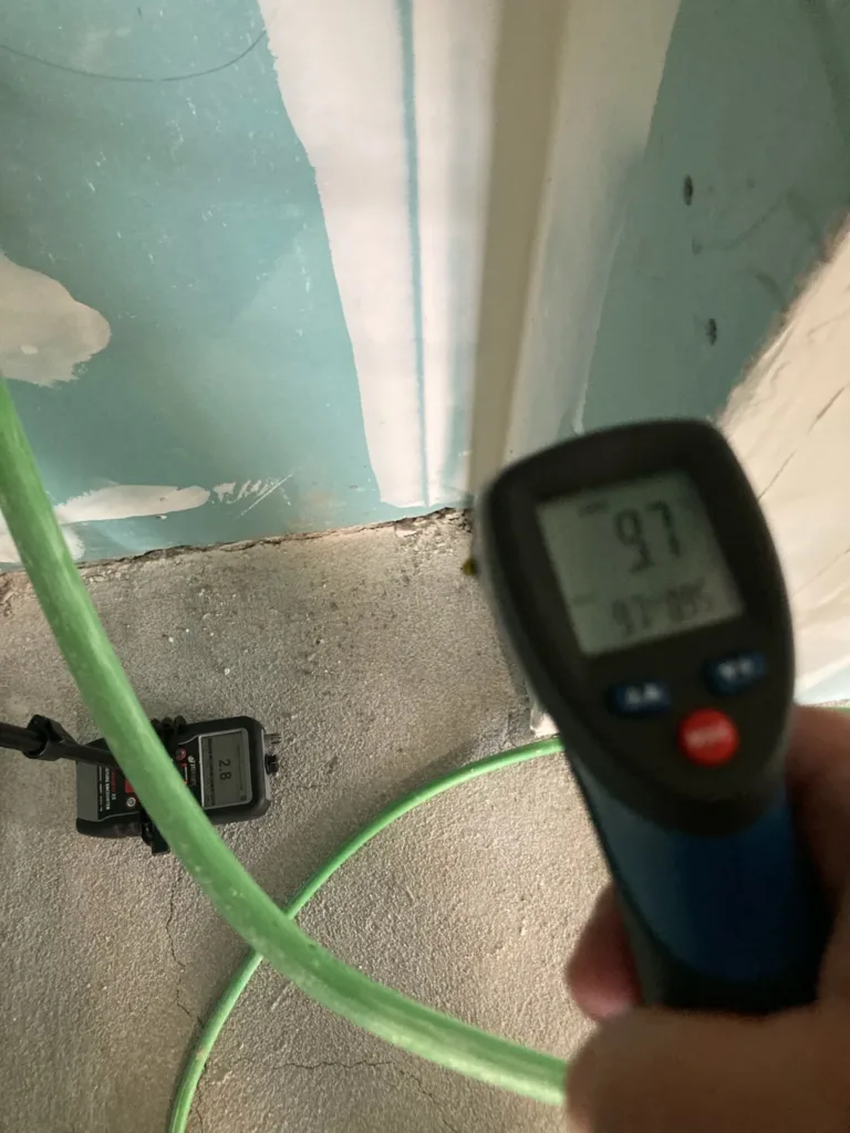 Termómetro de infrarrojos con 9,7 °C en la solera junto a un tabique y medidor de humedad no destructivo con una lectura de 2,8