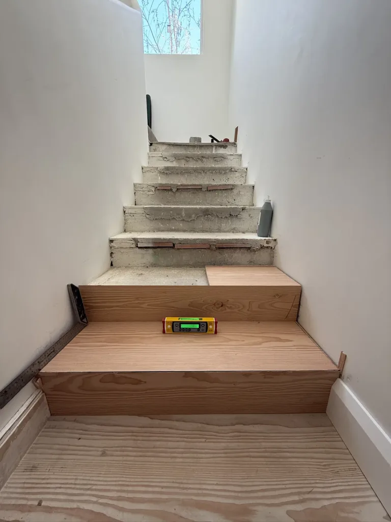 Escalera de obra con los primeros peldaños ya revestidos de huella y tabica de Douglas; un nivel descansa sobre una huella y los peldaños de arriba siguen en hormigón