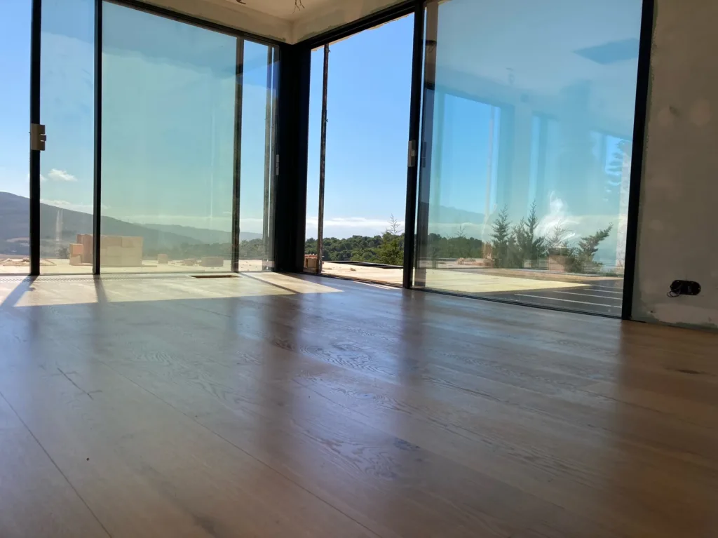 Salón acristalado en esquina con suelo Dinesen HeartOak de 300 mm y rejilla de clima de madera junto a la cristalera, vivienda en Betijuelo (Tarifa)