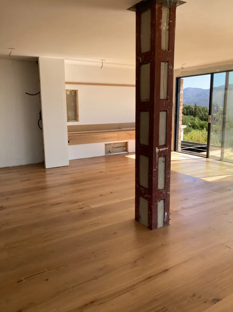Sala con pilar metálico sin revestir y suelo Dinesen HeartOak, abierta a la terraza con vistas a la sierra, vivienda en Betijuelo (Tarifa)