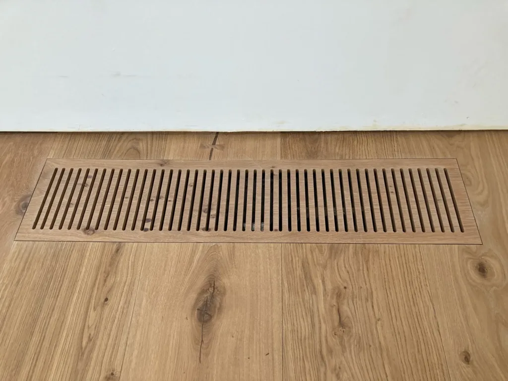 Rejilla de impulsión de clima mecanizada en CNC en la misma madera del suelo Dinesen HeartOak, junto a la pared