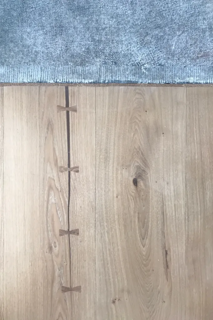 Grieta natural del duramen cosida con lazos de mariposa de roble en una tabla Dinesen HeartOak, en el encuentro con el pavimento contiguo, en ejecución