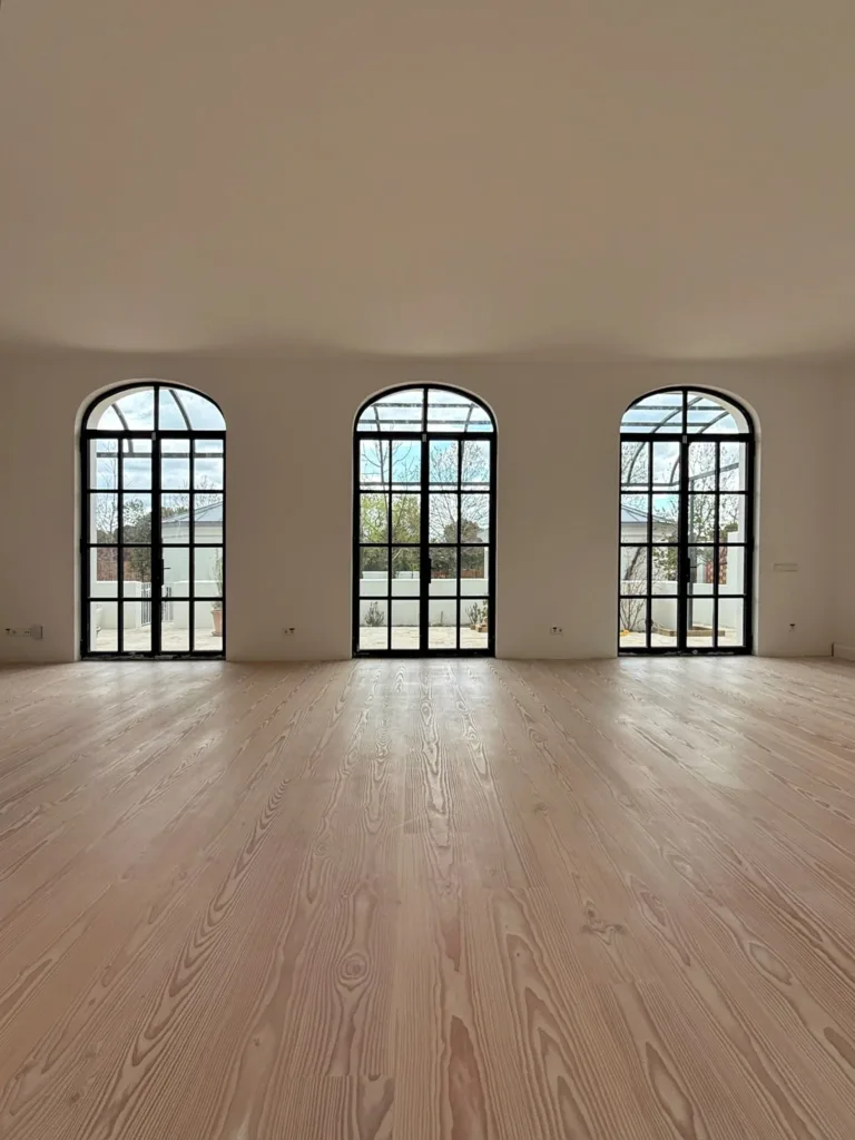 Salón con tres arcos de carpintería de acero al patio y suelo Dinesen Layers Douglas Classic con lejía y jabón blanco, vivienda en la calle Sigüenza (Madrid)