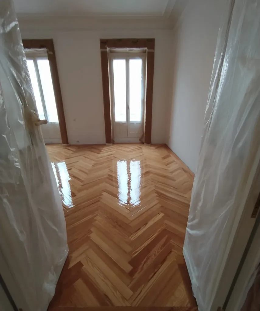 Dormitorio con dos balcones y la primera mano de barniz brillo recién dada sobre la espiga de pino melis viejo, vivienda en la calle Francisco de Rojas (Madrid)