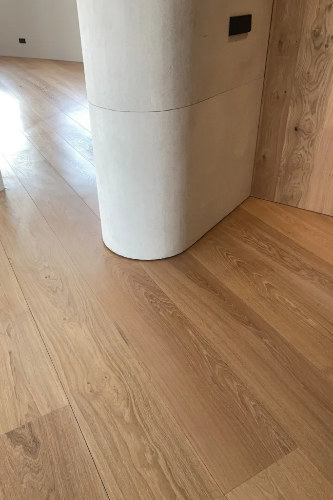 Suelo Dinesen Oak Classic recién instalado en torno a un pilar curvo de piedra, junto a un revestimiento de roble