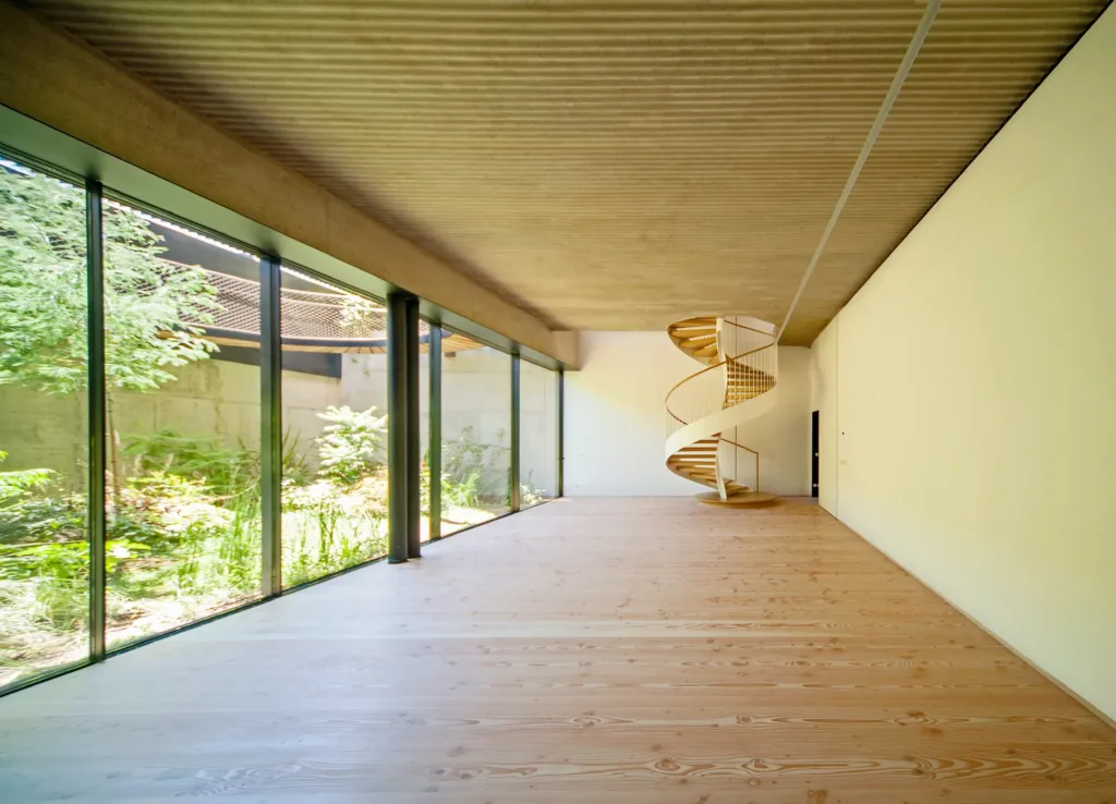 Salón acristalado al jardín de la planta sótano con suelo Dinesen Douglas de 350 mm y escalera de caracol al fondo, vivienda en Las Cárcavas (Madrid)