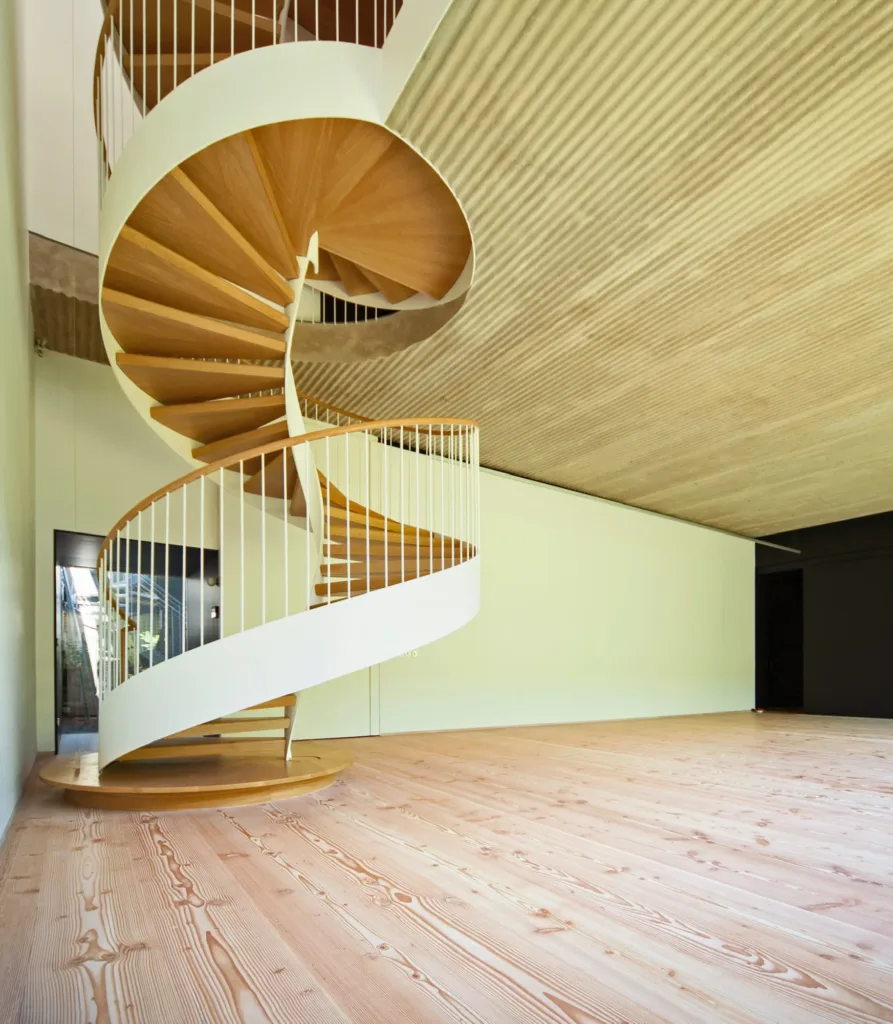 Escalera de caracol con peldaños de madera sobre el suelo Dinesen Douglas, vivienda en Las Cárcavas (Madrid)