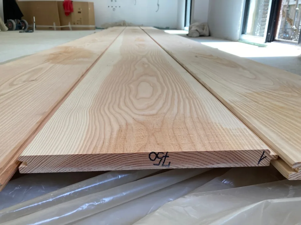 Tablas Dinesen Douglas Classic de 28 × 350 mm apiladas en obra, con el machihembrado a la vista