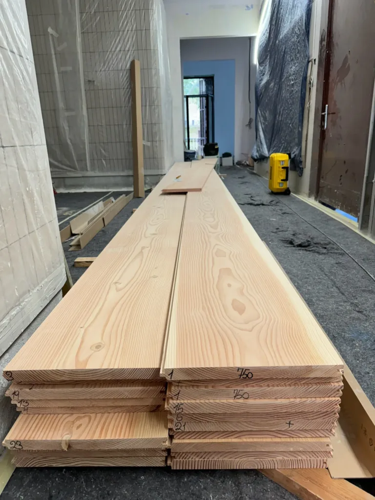 Tablas Dinesen Douglas Classic de 7,5 m apiladas sobre caballetes en la obra, con la longitud 750 marcada en el canto