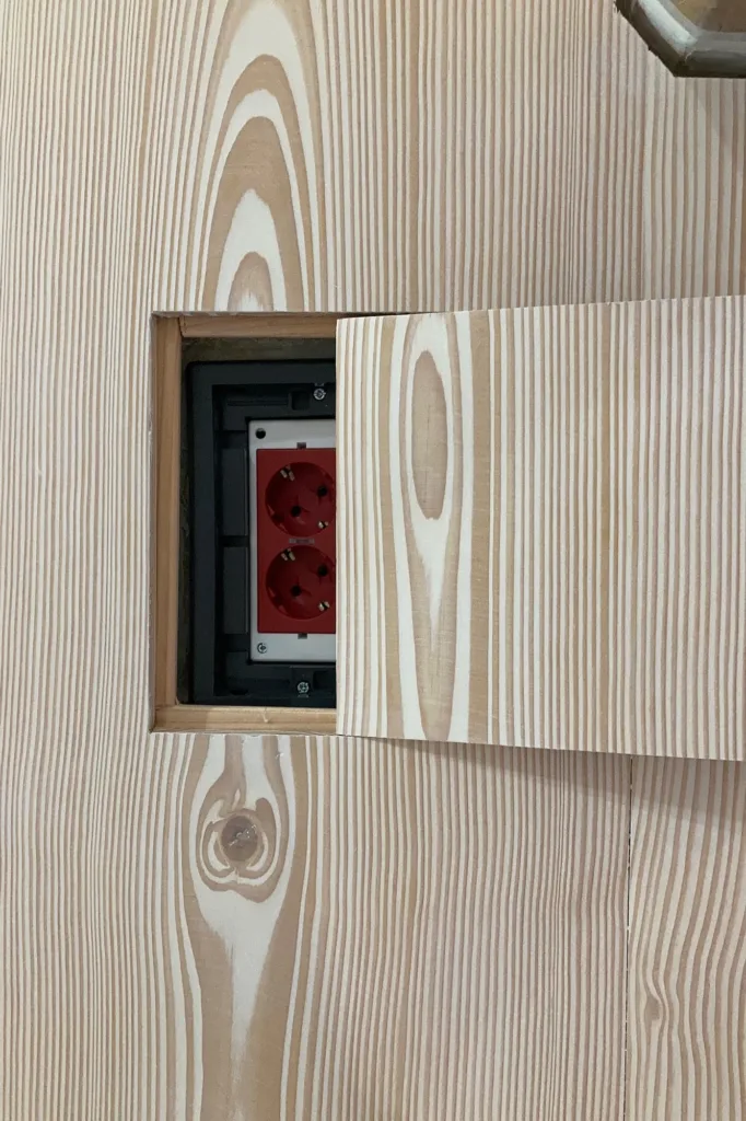 Registro abierto en el suelo Dinesen Douglas: caja de tomas de corriente bajo una tapa de la misma tabla