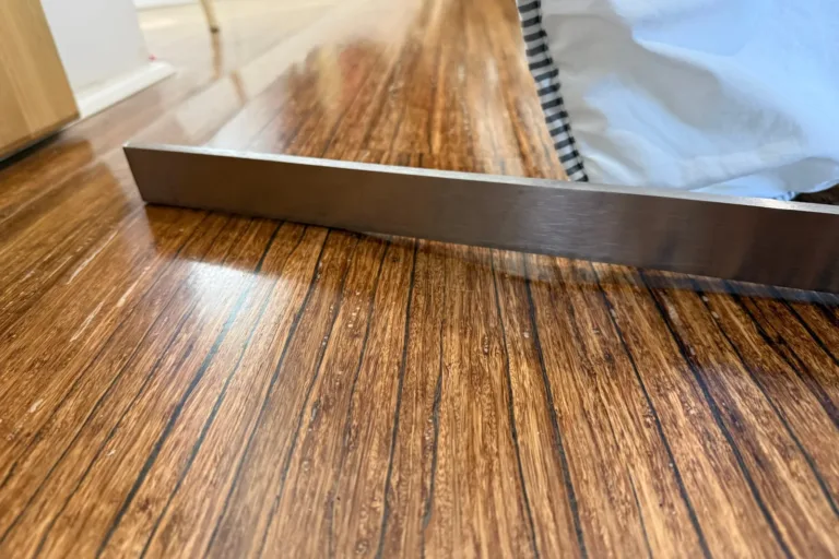 Regla de acero sobre varias tablas de bambú prensado onduladas tras una fuga, con puntos blancos en el acabado