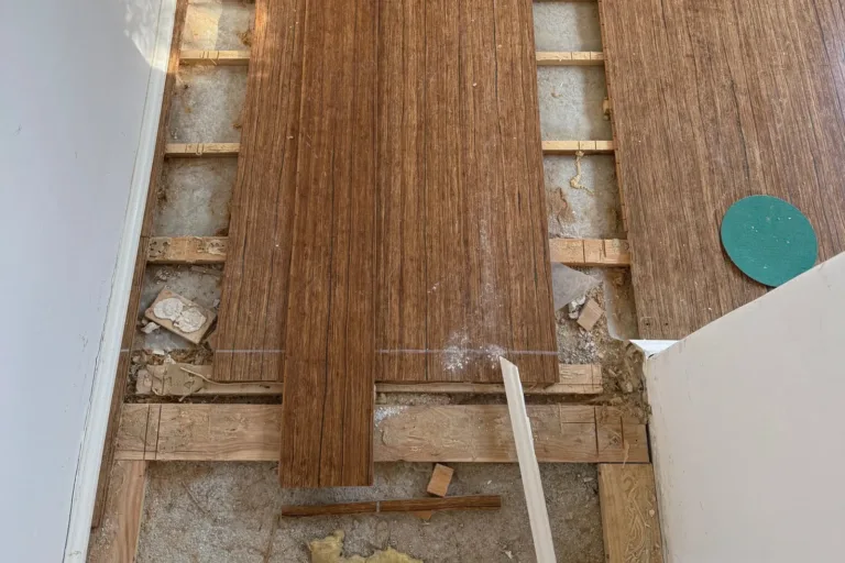 Suelo de bambú sobre rastreles abierto junto a la pared tras una fuga, con las tablas de la franja mojada retiradas