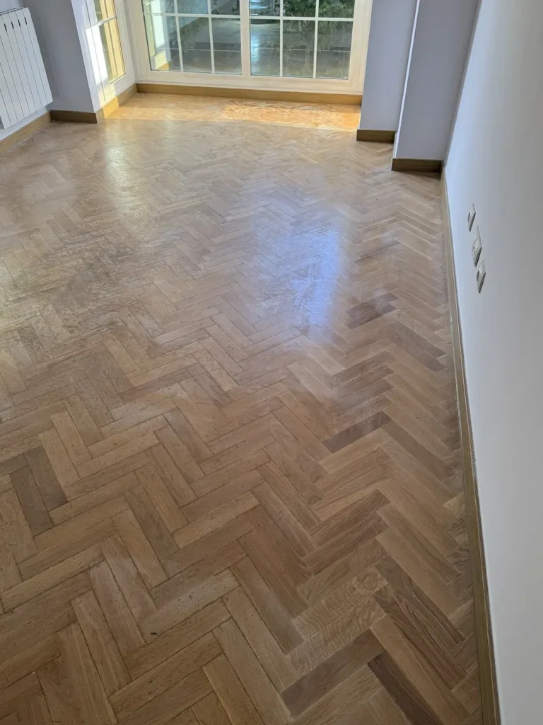 Parquet de roble en espiga antes del lijado: barniz gastado en la zona de paso y brillo solo junto a la pared, piso con mirador en Madrid