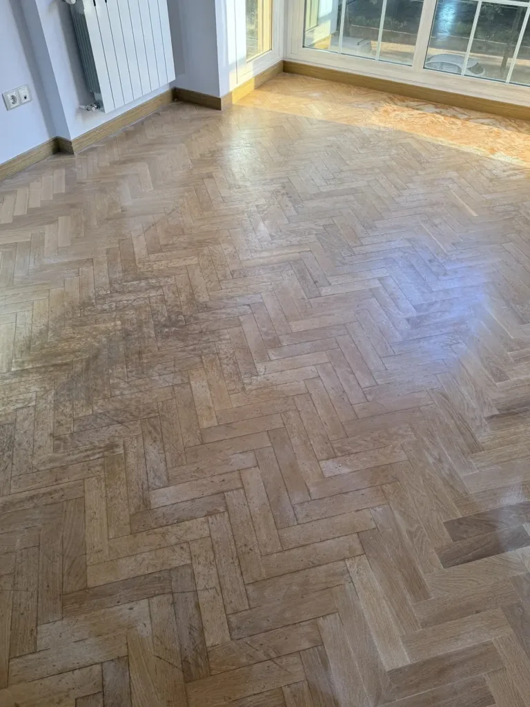 Parquet de roble en espiga antes del lijado, con el barniz antiguo amarilleado y gastado junto al mirador, piso con mirador en Madrid