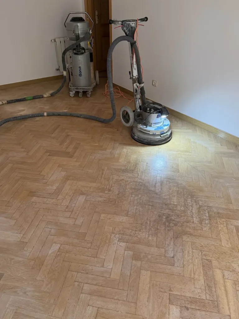 Lijadora Bona FlexiSand trabajando junto a la pared sobre el parquet de roble en espiga, con el aspirador Bona DCS 70 al fondo, piso con mirador en Madrid