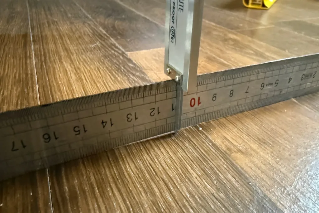 Regla de acero sobre un parquet y pie de rey con sonda de profundidad midiendo la flecha bajo la regla