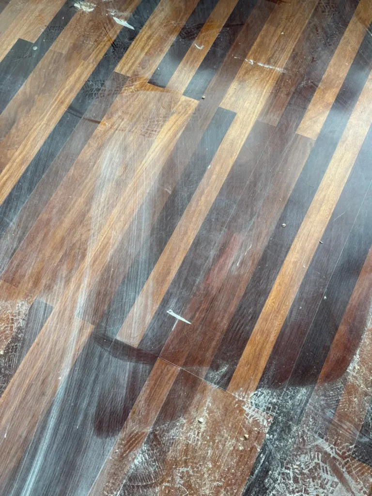 Parquet de maderas tropicales de varios tonos, con el barniz anterior rayado y polvo de obra encima, antes de la restauración