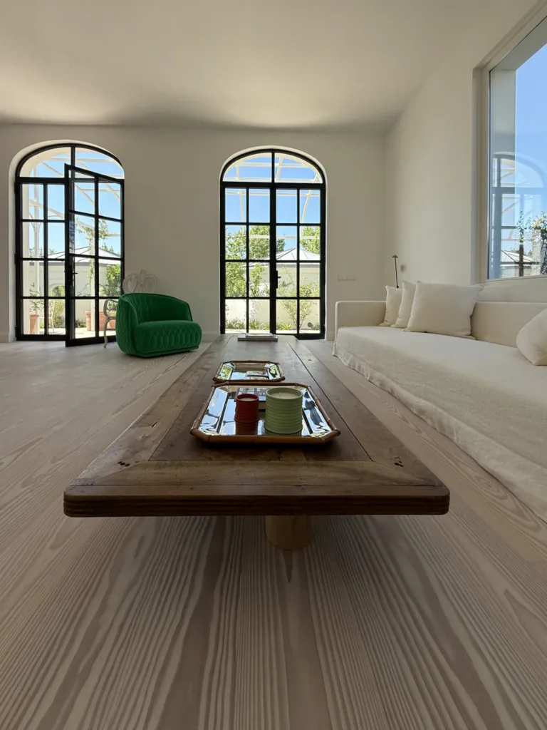 Salón con dos ventanales de arco, sofá blanco y mesa baja de madera sobre suelo Dinesen Layers Douglas