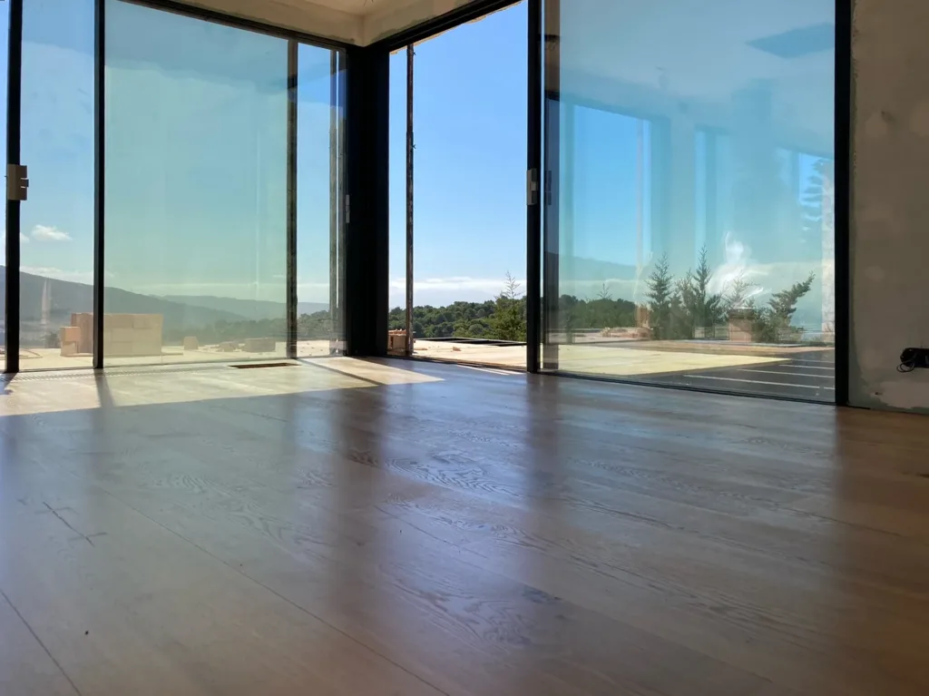 Salón acristalado en esquina con suelo Dinesen HeartOak de 300 mm y rejilla de clima de madera junto a la cristalera, vivienda en Betijuelo (Tarifa)