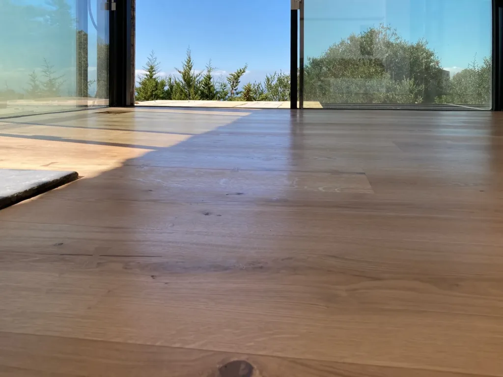 Suelo de madera Dinesen HeartOak a ras de la cristalera abierta, con el pinar y el mar al fondo, vivienda en Betijuelo (Tarifa)