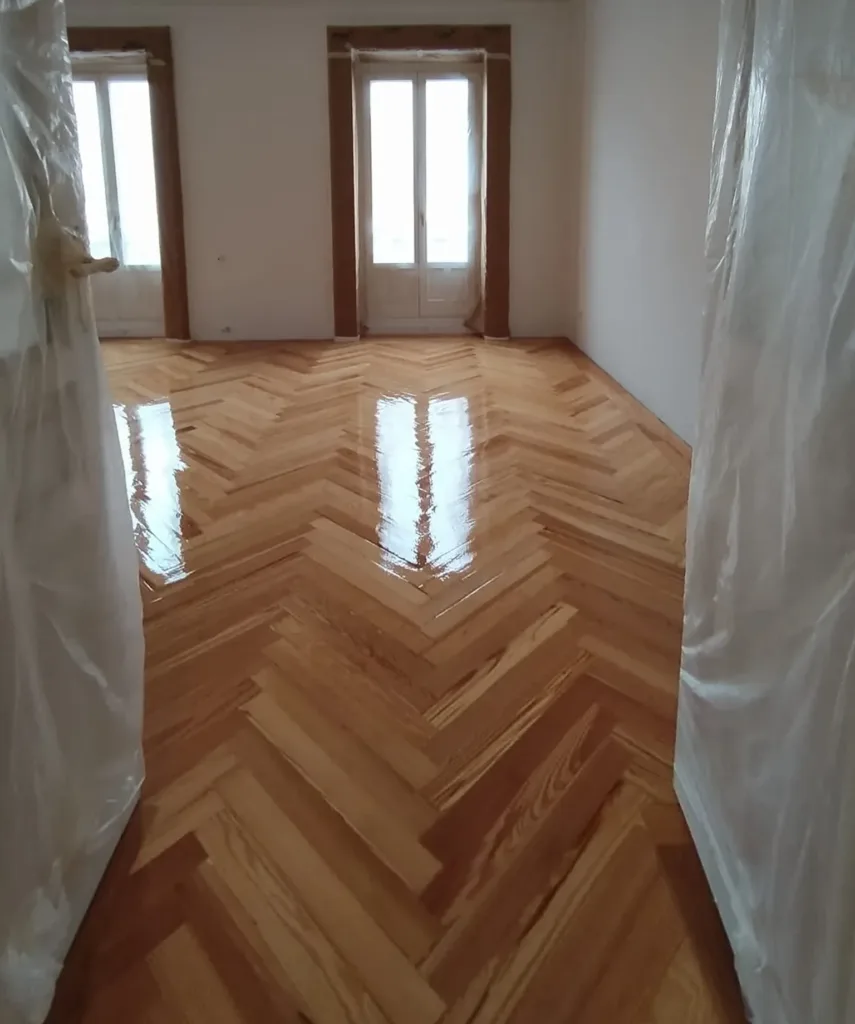 Dormitorio con dos balcones y la primera mano de barniz brillo recién dada sobre la espiga de pino melis viejo, vivienda en Chamberí (Madrid)