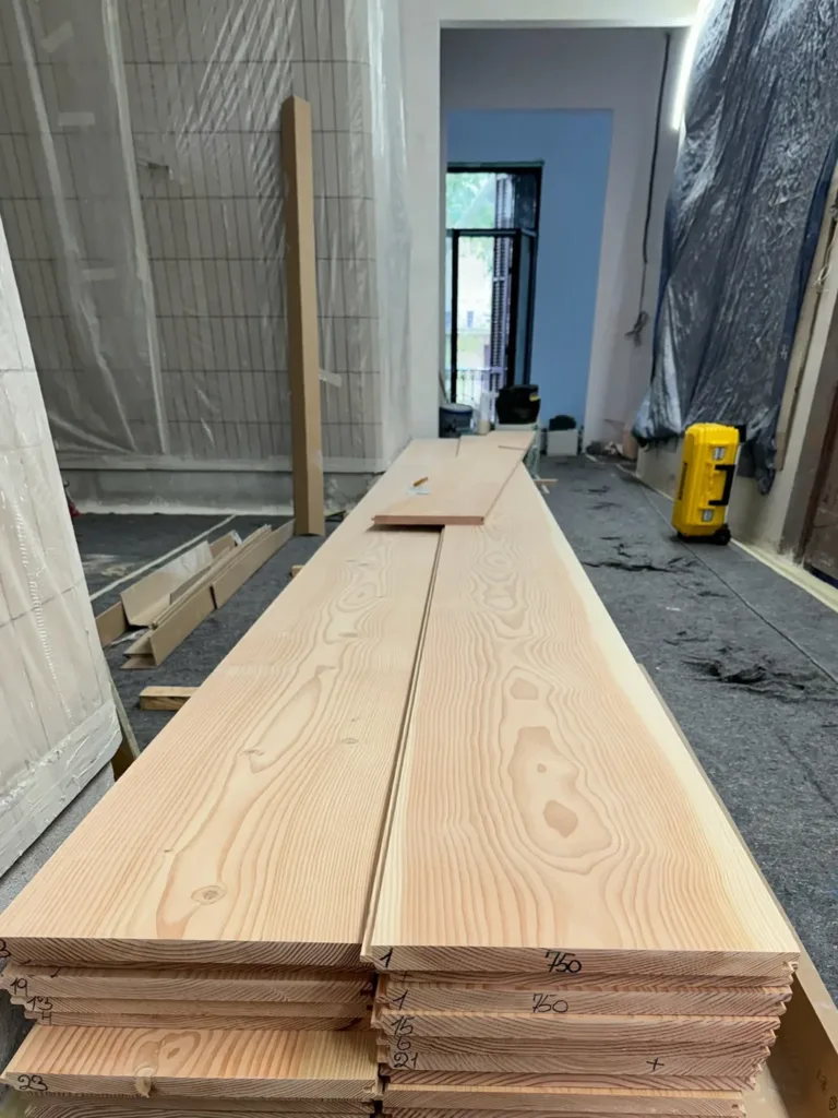Tablas Dinesen Douglas Classic de 7,5 m apiladas sobre caballetes en la obra, con la longitud 750 marcada en el canto